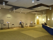 Image of lobby space with 3 tall tables and chairs, and registration tables along a wall.