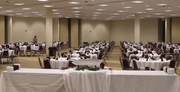 Image of conference hall with buffet table in the foreground and rows of round table seating for guests.